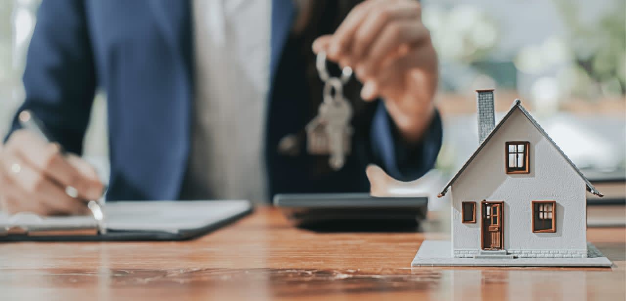 Small house model and a man holding keys in the background