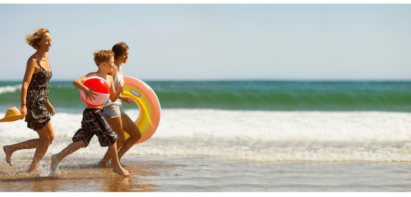 A mother and her son and daughter running at the beach